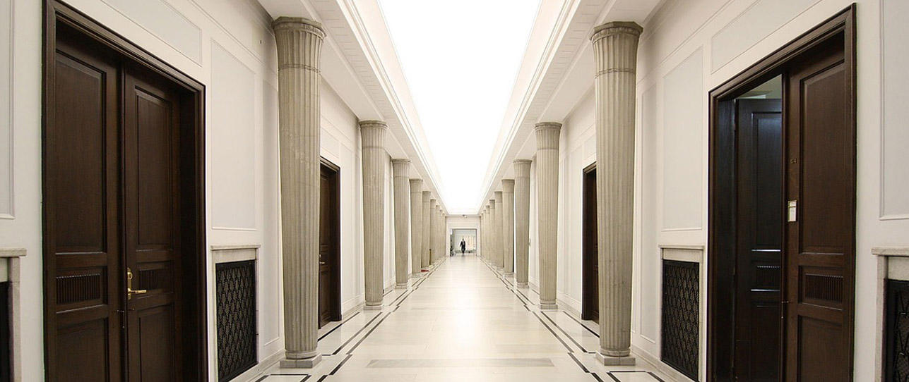 An empty white corridor with dark brown doors and white columns in a modern building.