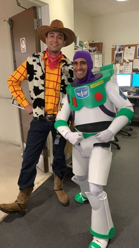 Two people wearing Buzz Lightyear and Woody costumes posing in an office.